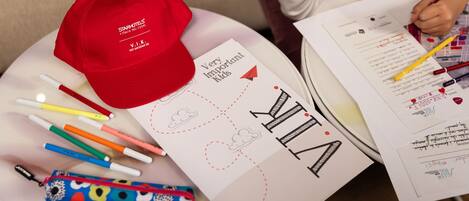 Una mesa con un tapete rojo, varios bolígrafos, un estuche para lápices y papeles con dibujos y escritura.