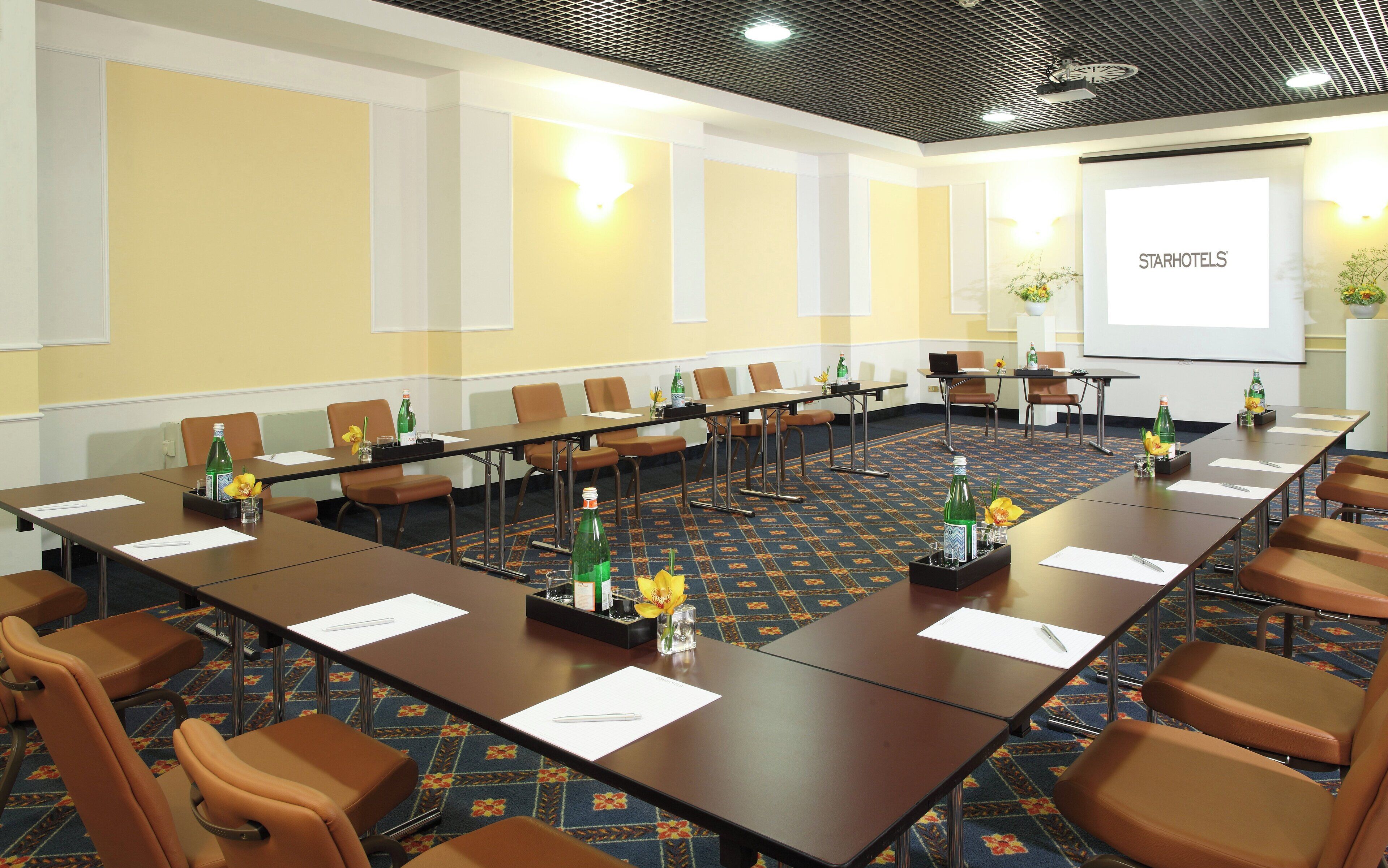 A conference room with a long table, multiple chairs, and a projector screen displaying "STARHOTELS".