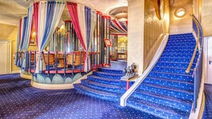A grand staircase with blue carpet and a red railing, leading to a balcony with colorful drapes. - Auriga Hotel (Milan)