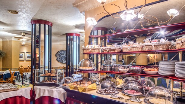 A buffet setup with various food items and baskets, a chandelier, and a clock on the wall. - Auriga Hotel (Milan)