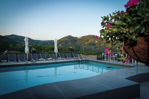 Una piscina al aire libre, sombrillas, sillones reclinables de piscina