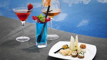 A poolside setting with three cocktails and a plate of appetizers.
