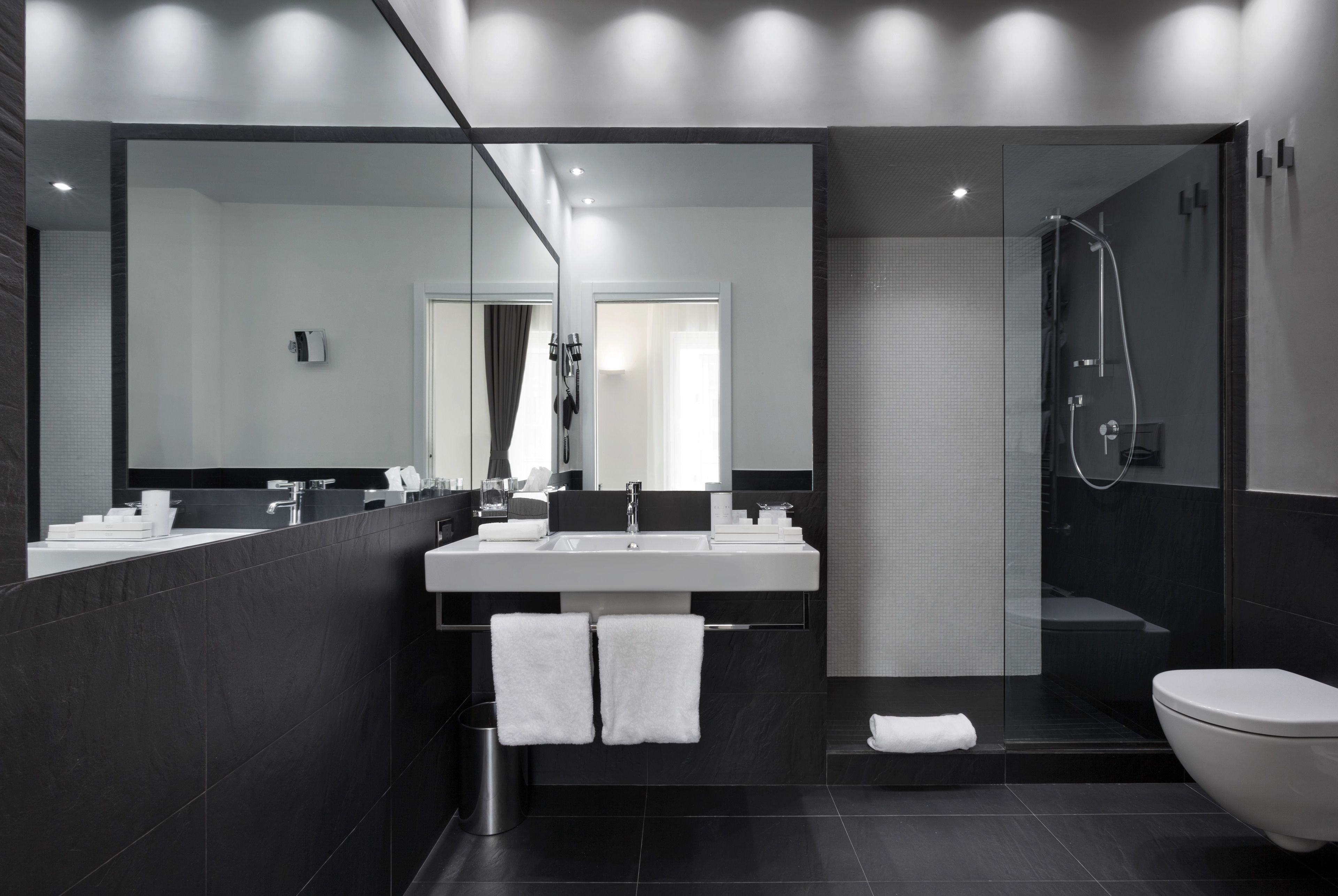 A modern bathroom with a large mirror, dual sinks, a shower, and a toilet.
