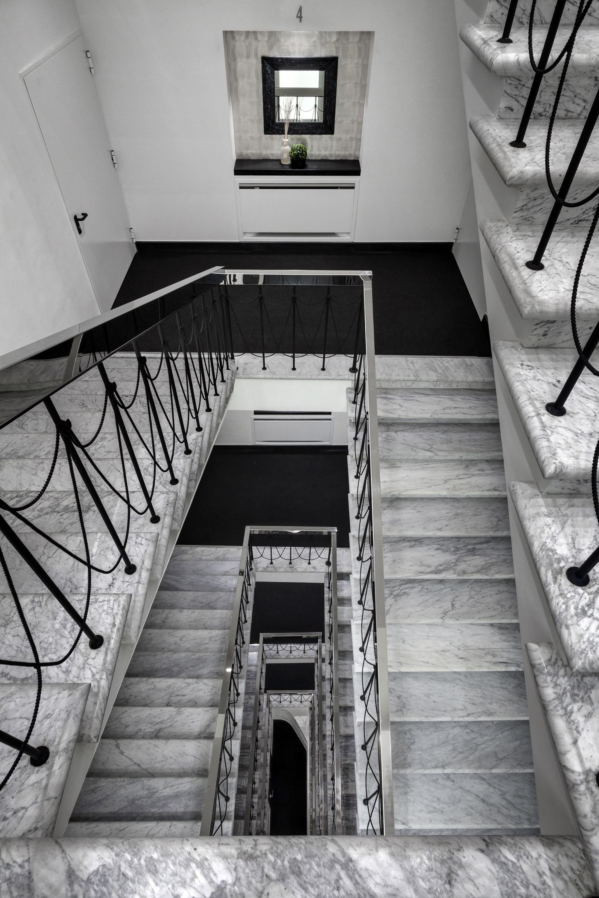 A modern staircase with marble steps and metal railings, leading to a landing with a small window and a plant.