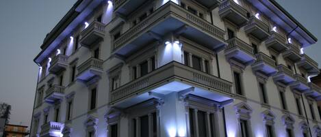 A multi-story building with classical architecture, featuring balconies and illuminated windows.