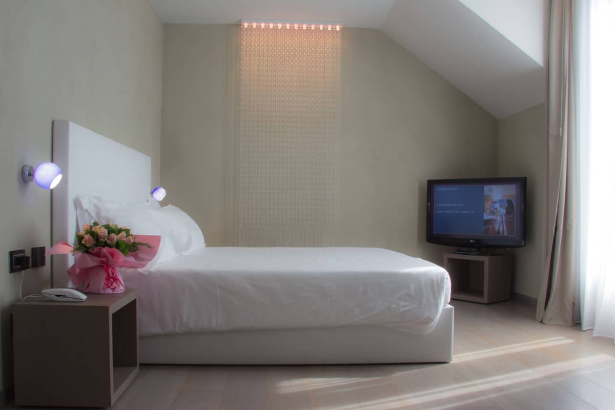 Une chambre d’hôtel moderne avec un grand lit, une table de chevet avec une lampe, une télévision et un bouquet de fleurs.