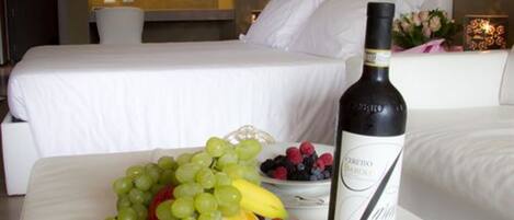 A hotel room with a bed, a bedside table with a bottle of wine, and a plate of fruit.