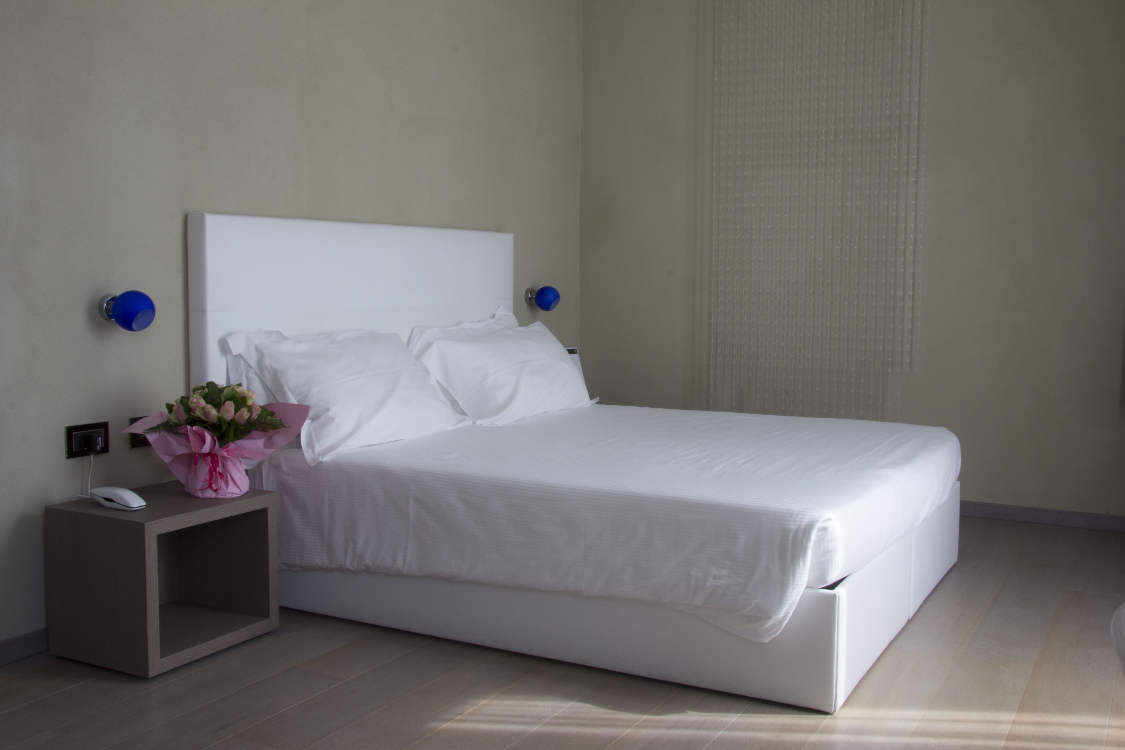 A neatly made bed with white linens in a room with light-colored walls and wooden flooring.