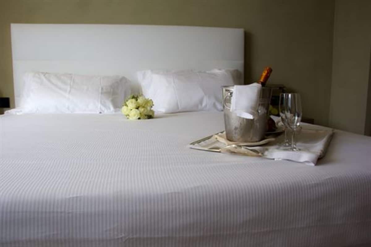 Un lit parfaitement fait, avec du linge de lit blanc, une bouteille de champagne et un verre sur un plateau.