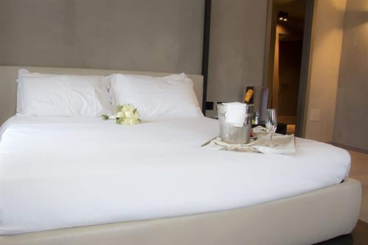 Un lit parfaitement fait, avec du linge de lit blanc, un bouquet de fleurs blanches et une bouteille de champagne posée à côté.