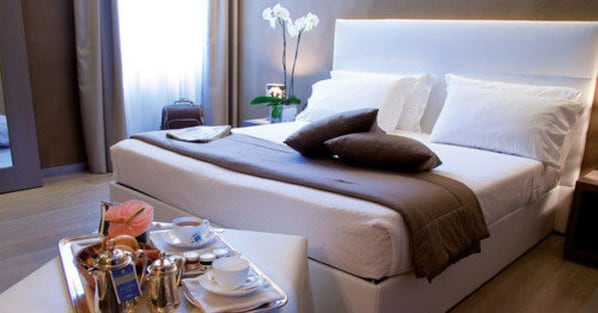 A neatly made bed with pillows, a bedside table with a tray of breakfast items, and a potted orchid.