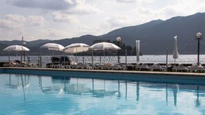 Una piscina amb gandules i ombrelles, vista al mar i muntanyes al fons.