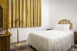A hotel room with a bed, a bedside table, a lamp, and a curtain.