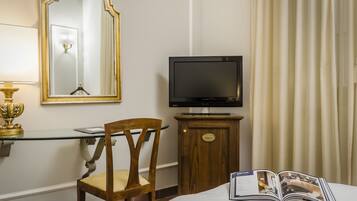 Una camera d'albergo con televisore su un mobile in legno, uno specchio a parete, una sedia e un letto con una rivista.