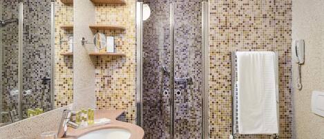 Un baño con ducha revestida de mosaicos, un lavabo con artículos de aseo y una toalla colgada en la pared.