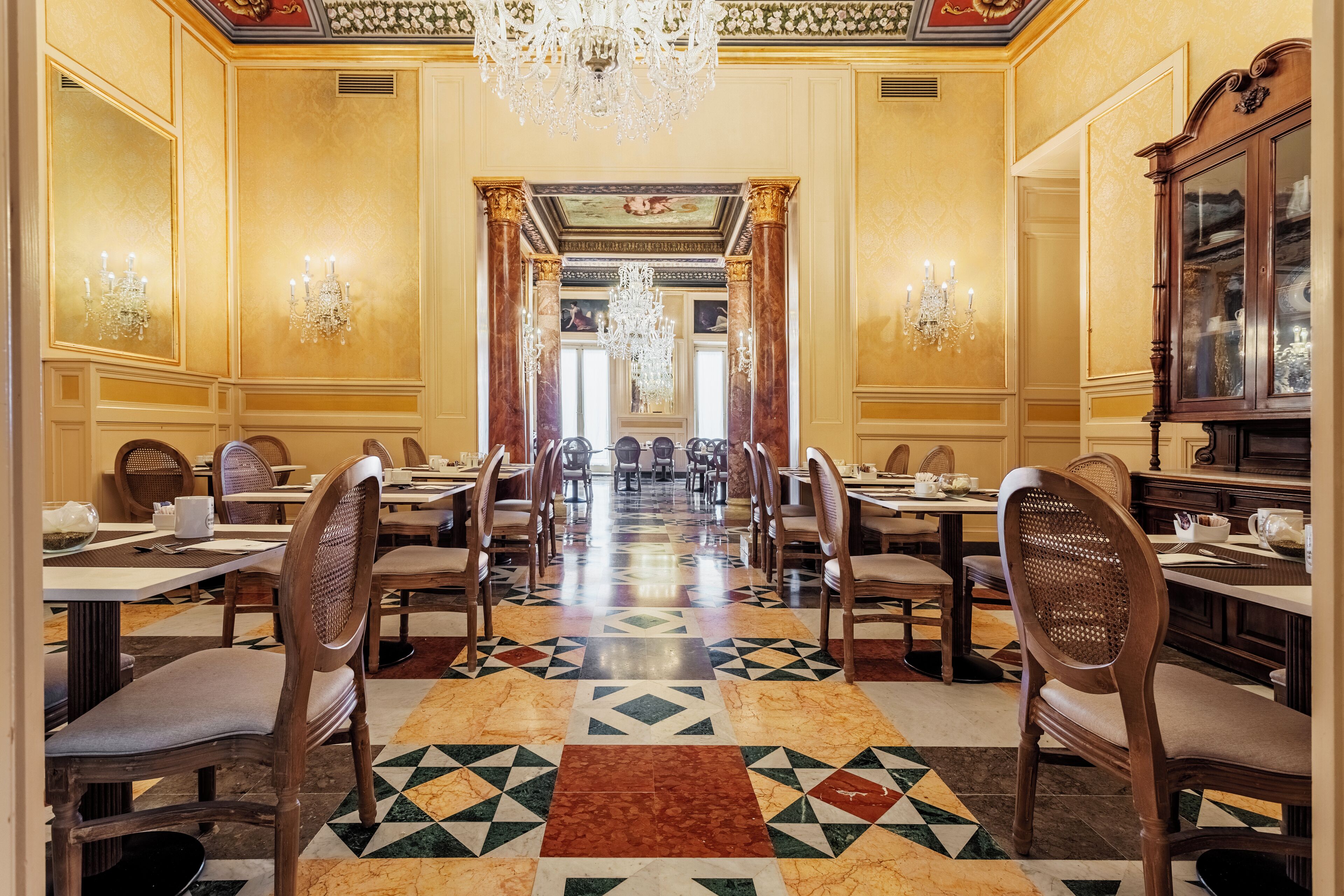 Une salle à manger élégante, avec une longue table, des chaises, des lustres et un sol à motifs.