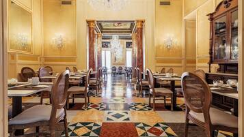 Une salle à manger élégante, avec une longue table, des chaises, des lustres et un sol à motifs.
