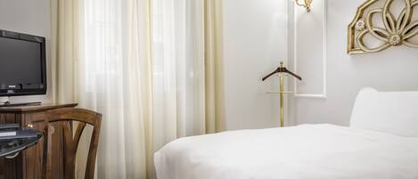 Ein Hotelzimmer mit Bett, Schreibtisch mit Fernseher, Stuhl, Kleiderschrank und Wandleuchte.