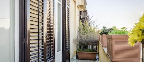 A narrow outdoor corridor with a tiled floor, a door with a metal handle, and a window with horizontal blinds.