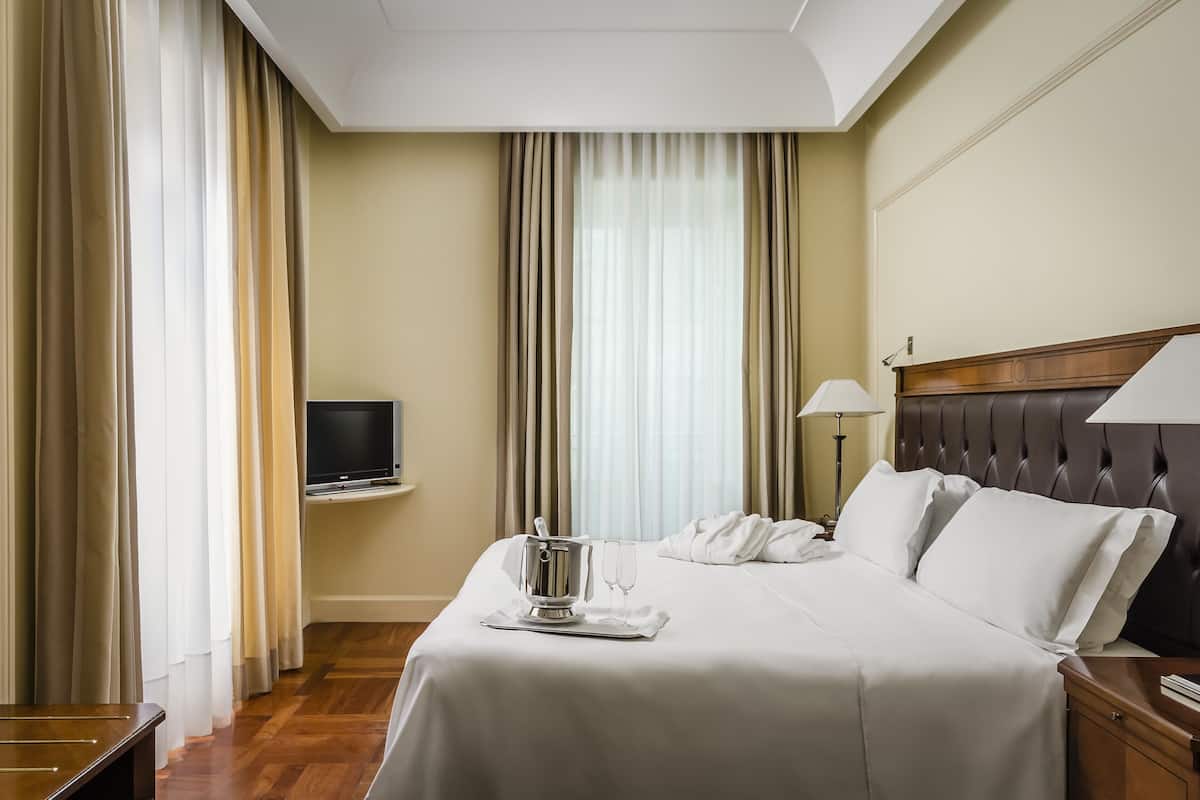 A hotel room with a bed, a TV, a minibar, and curtains.