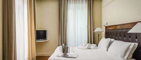 A hotel room with a bed, a TV, a minibar, and curtains.