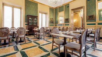 A dining area with multiple tables and chairs, a chandelier, and green patterned walls.