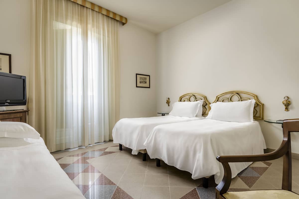 A hotel room with two beds, a television, a chair, and a large window with curtains.