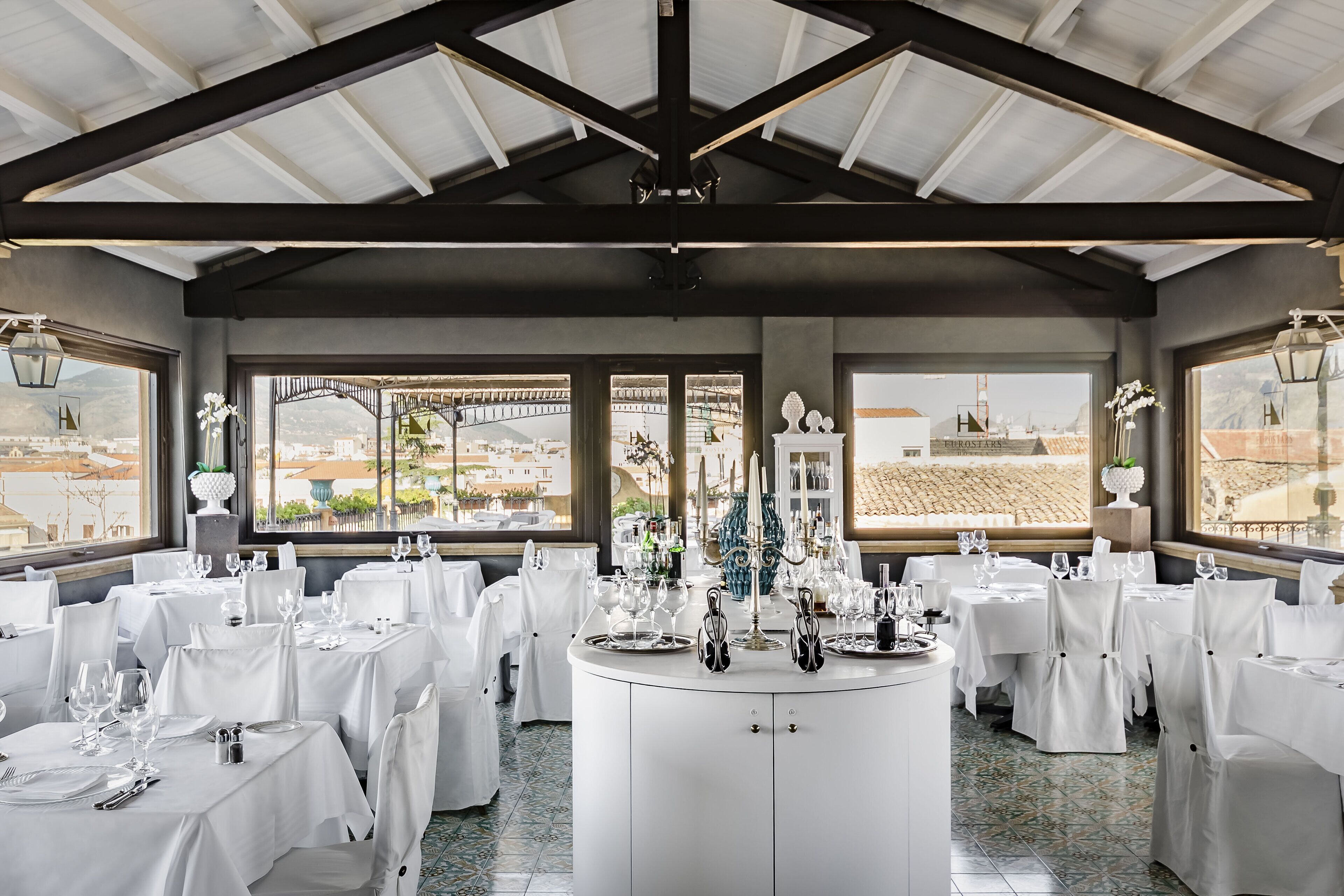 A restaurant with white tablecloths, round tables, and a central island with a vase and candles.