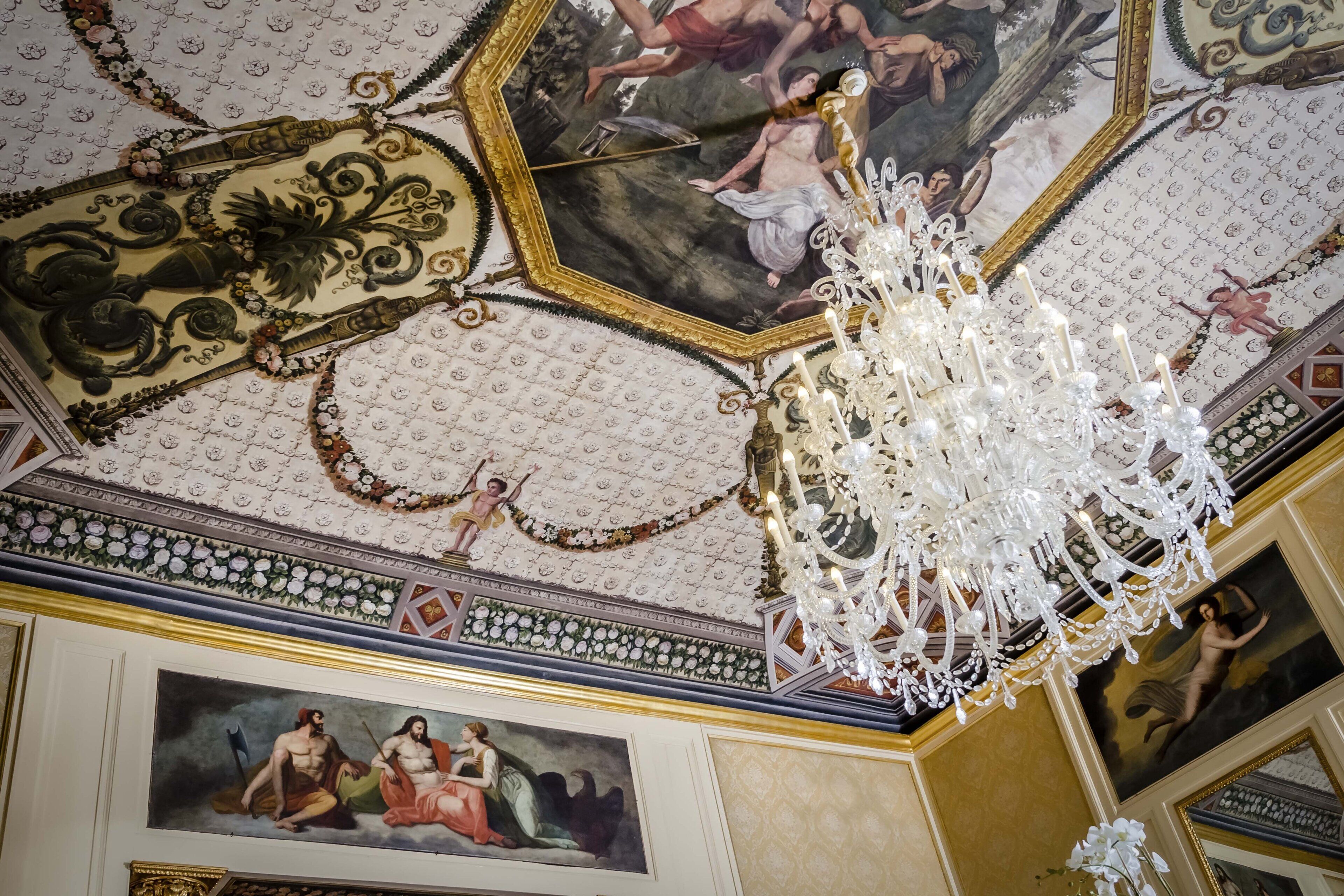 Un soffitto con decorazioni elaborate, un lampadario e dipinti classici.