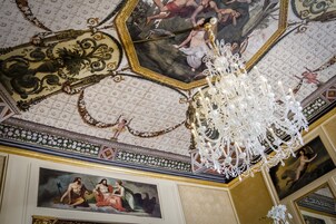 Un soffitto con decorazioni elaborate, un lampadario e dipinti classici.