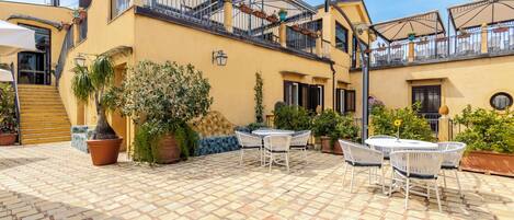 Un patio con suelo de baldosas, mobiliario exterior y plantas en macetas.