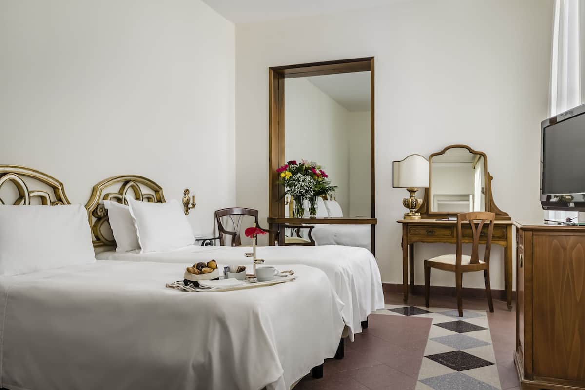 A hotel room with two beds, a desk with a chair, a television, and a large mirror.