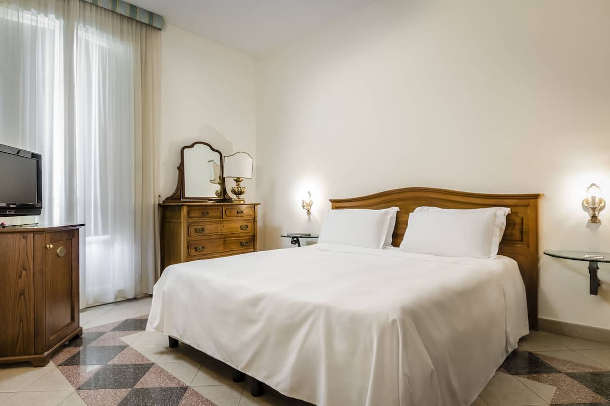 A hotel room with a large bed, wooden dresser, television, and a mirror.