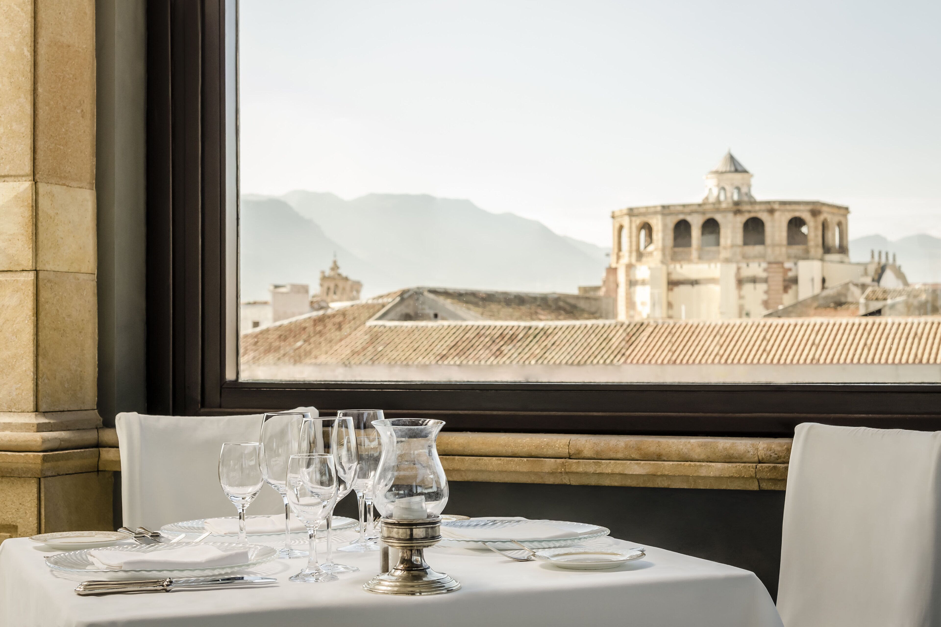 A dining table set with plates, glasses, and cutlery, with a view of a historic building through a window.