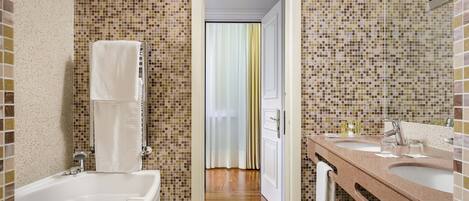 A bathroom with a mosaic tile wall, a bathtub, a sink with a mirror, and a door leading to another room.