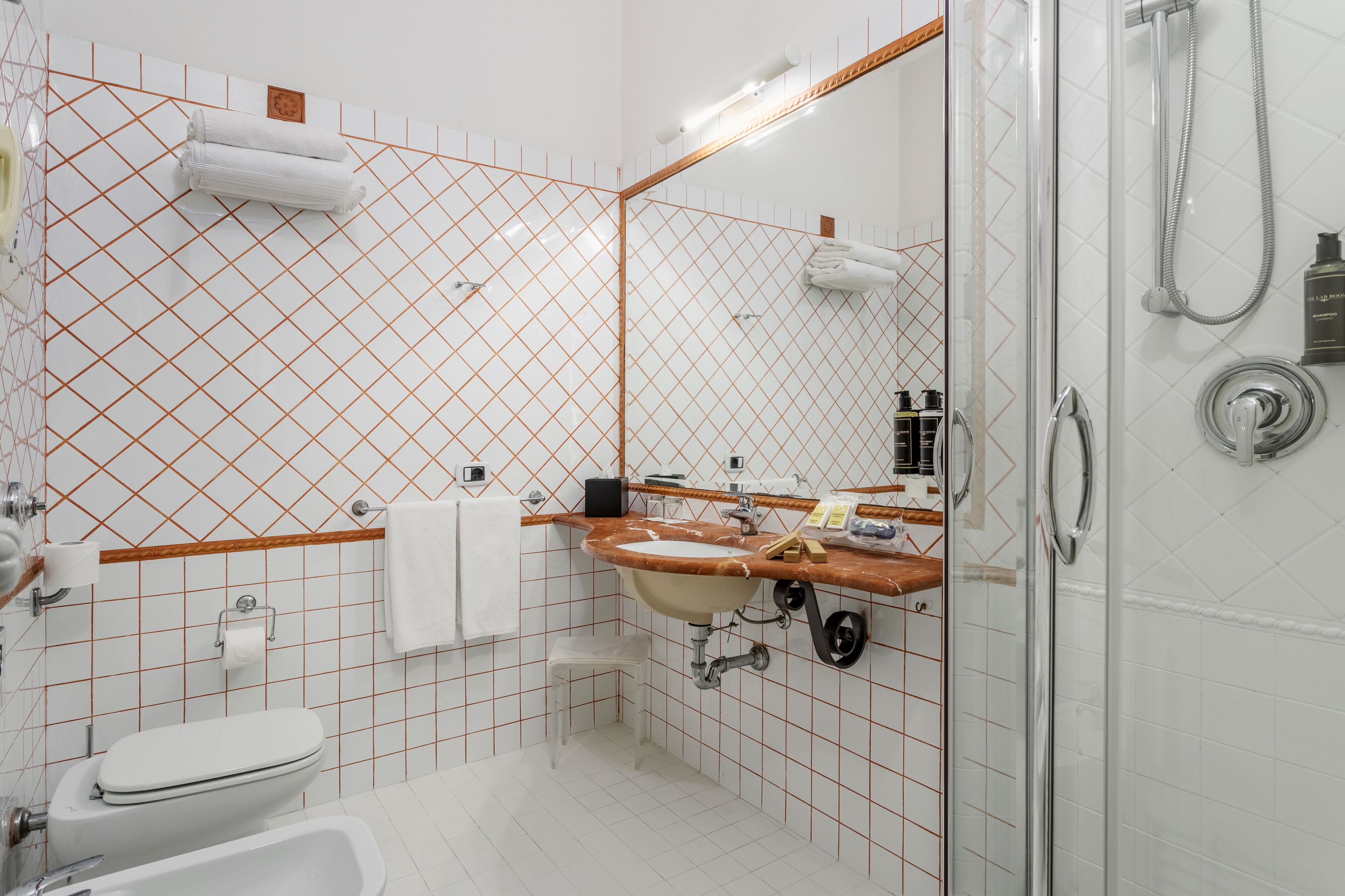 A bathroom with a white toilet, sink, and shower. There are towels hanging on the wall and a mirror above the sink.