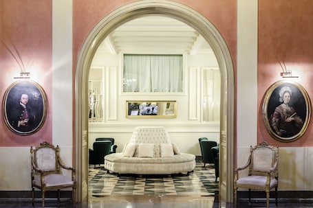 A grand lobby with a large arched doorway, a tufted sofa, and two ornate chairs.