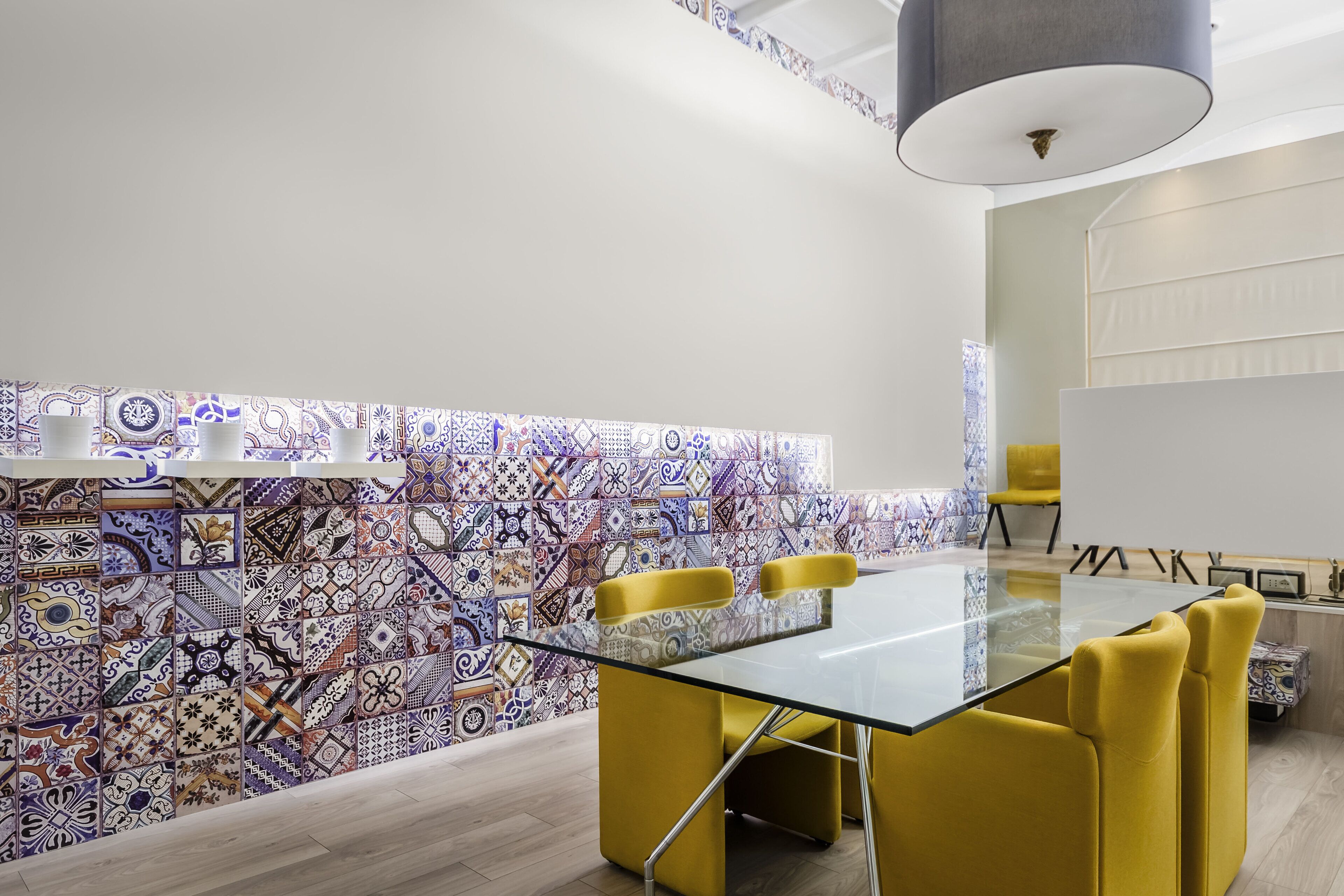A modern meeting room with a glass table, yellow chairs, patterned tile walls, and a ceiling light.