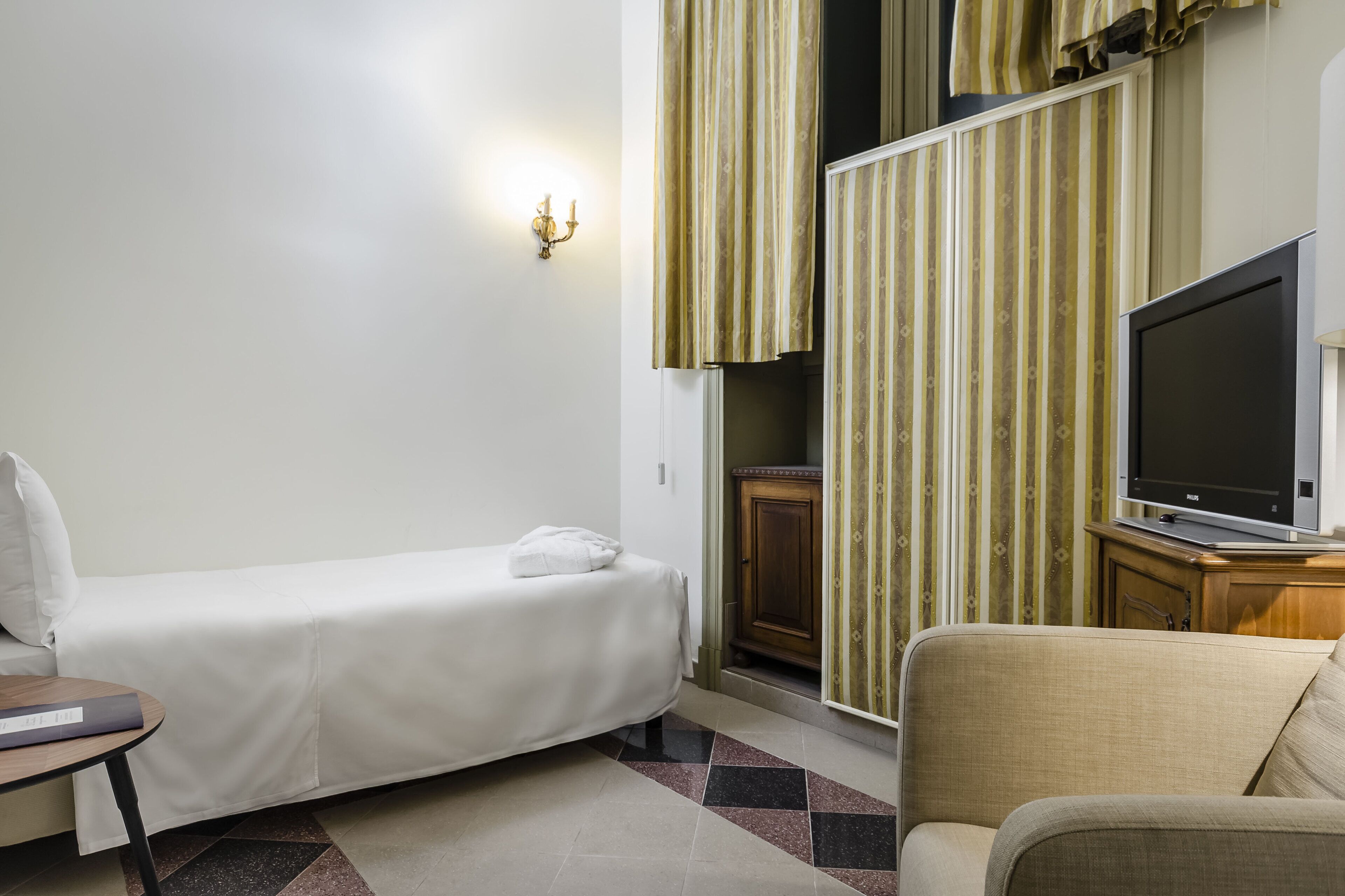 Une petite pièce, bien rangée, comprenant un lit simple, un canapé, un téléviseur et un meuble.