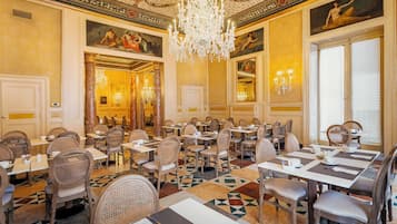 Ein formeller Speisesaal mit mehreren Tischen und Stühlen, einer Kristallleuchter und klassischen Wandmalereien.