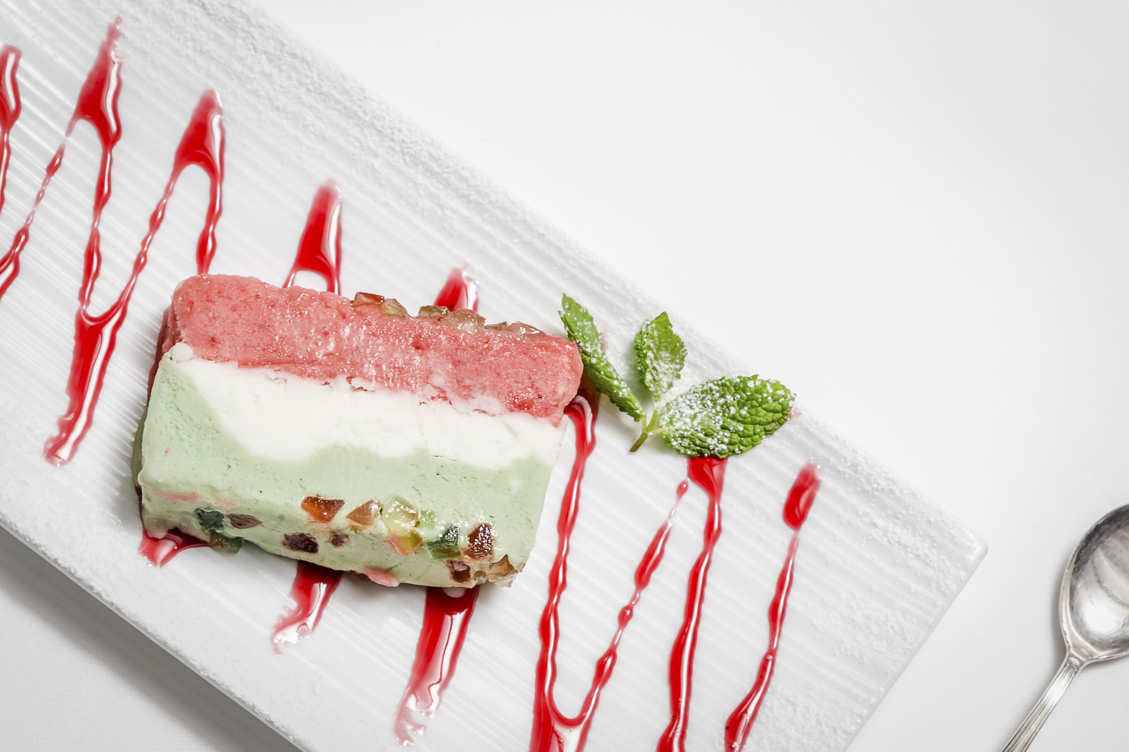 A dessert on a white plate with red syrup and mint leaves.