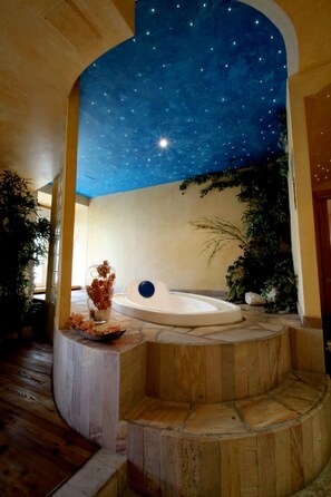 A circular hot tub with a starry ceiling, surrounded by stone steps and potted plants. - Grande Albergo (Roccaraso)