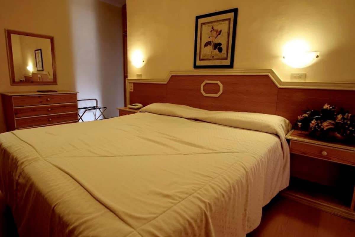 A hotel room with a large bed, a dresser, a mirror, a nightstand, and a framed picture on the wall.