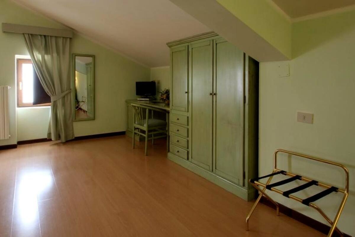 A room with a wooden floor, a green wardrobe, a desk with a computer, and a bench.