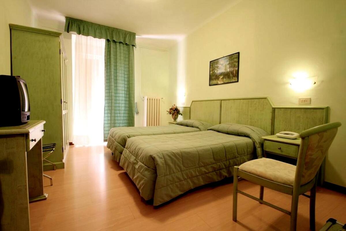 A room with two beds, a chair, a desk with a telephone, and a painting on the wall.