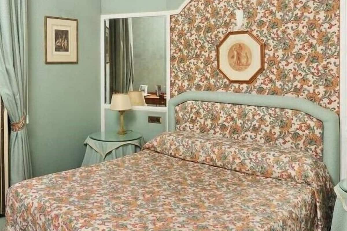 A bedroom with a floral-patterned headboard, a bed with a matching floral bedspread, a bedside table, and a mirror.