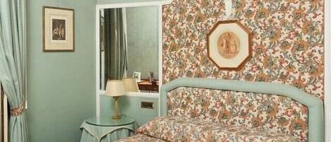 Une chambre à coucher avec une tête de lit à motifs floraux, un lit avec une couvre-lit assortie, une table de chevet et un miroir.