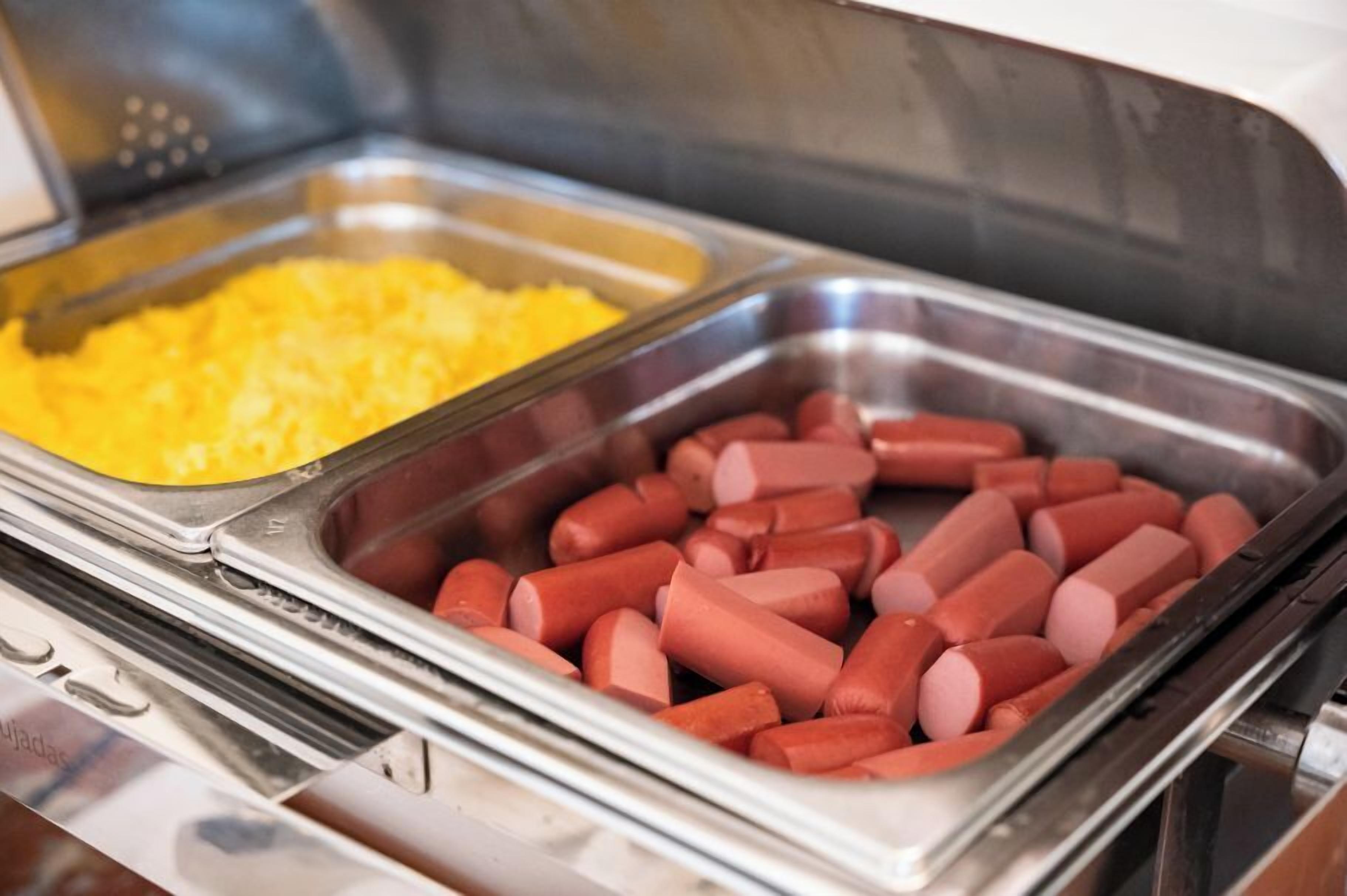 A buffet with two trays, one containing scrambled eggs and the other containing hot dogs.