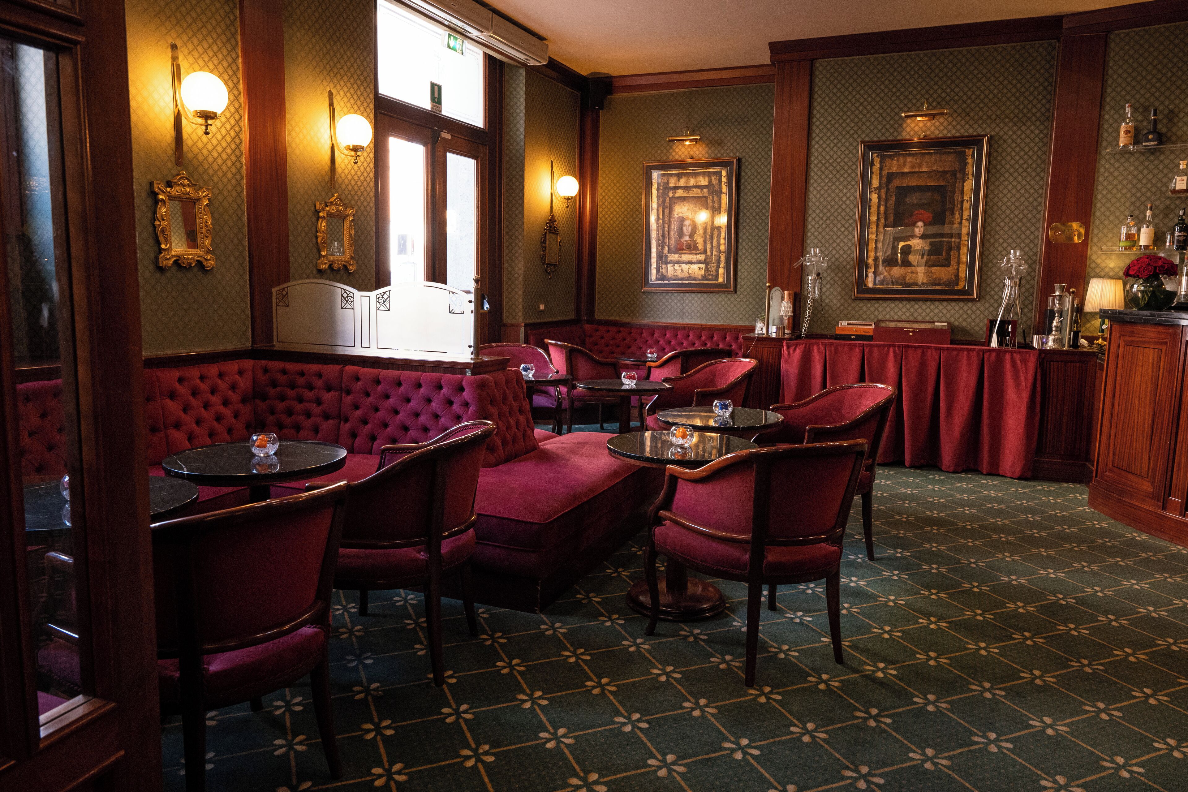 Un restaurante acogedor con asientos tapizados en rojo, mesas de madera y alfombra estampada.