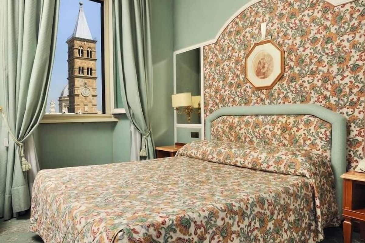A room with a bed, a nightstand, a lamp, and a window with curtains.
